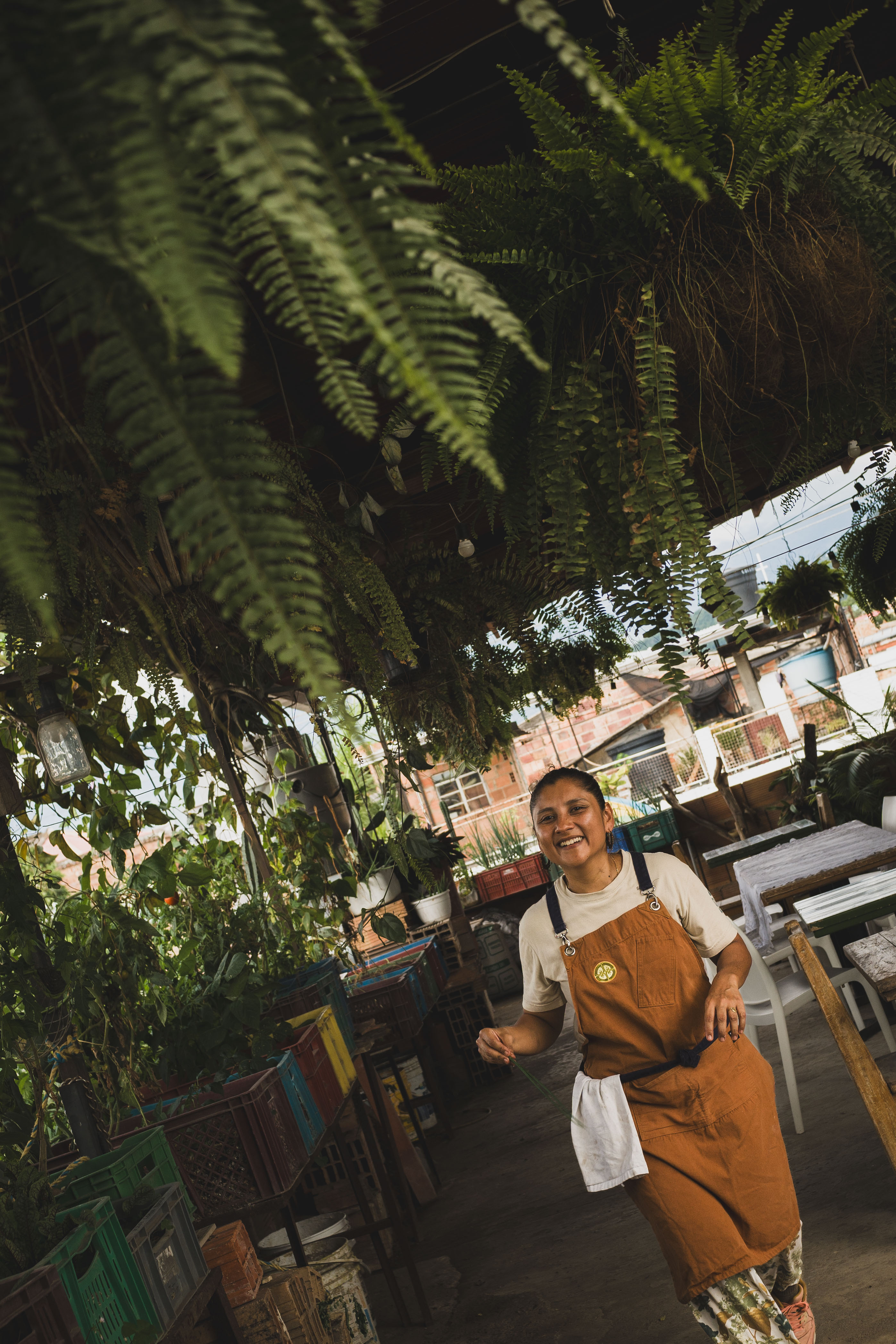 Una cocinera sonríe en una terraza cubierta de helechos y plantas.