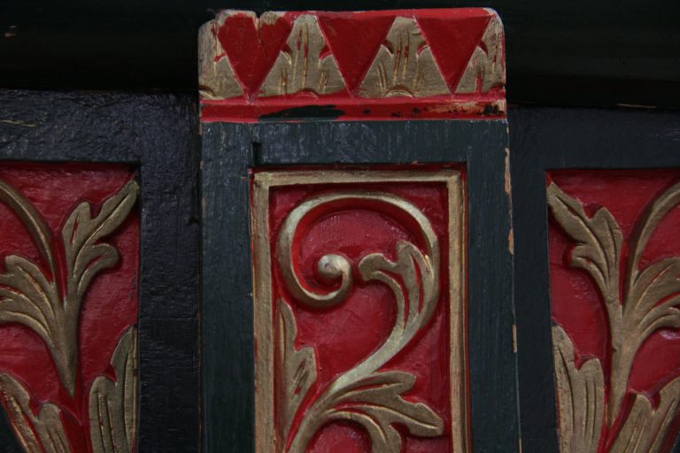 Detalle de la columna del soporte con paneles tallados en rojo, negro y dorado.