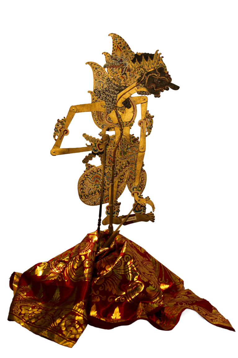 Figura de wayang kulit calada y policromada, sobre un textil rojo y dorado.