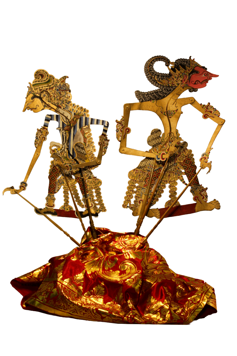Dos figuras de wayang kulit sobre textil rojo y dorado, con sus sombras en la pared.