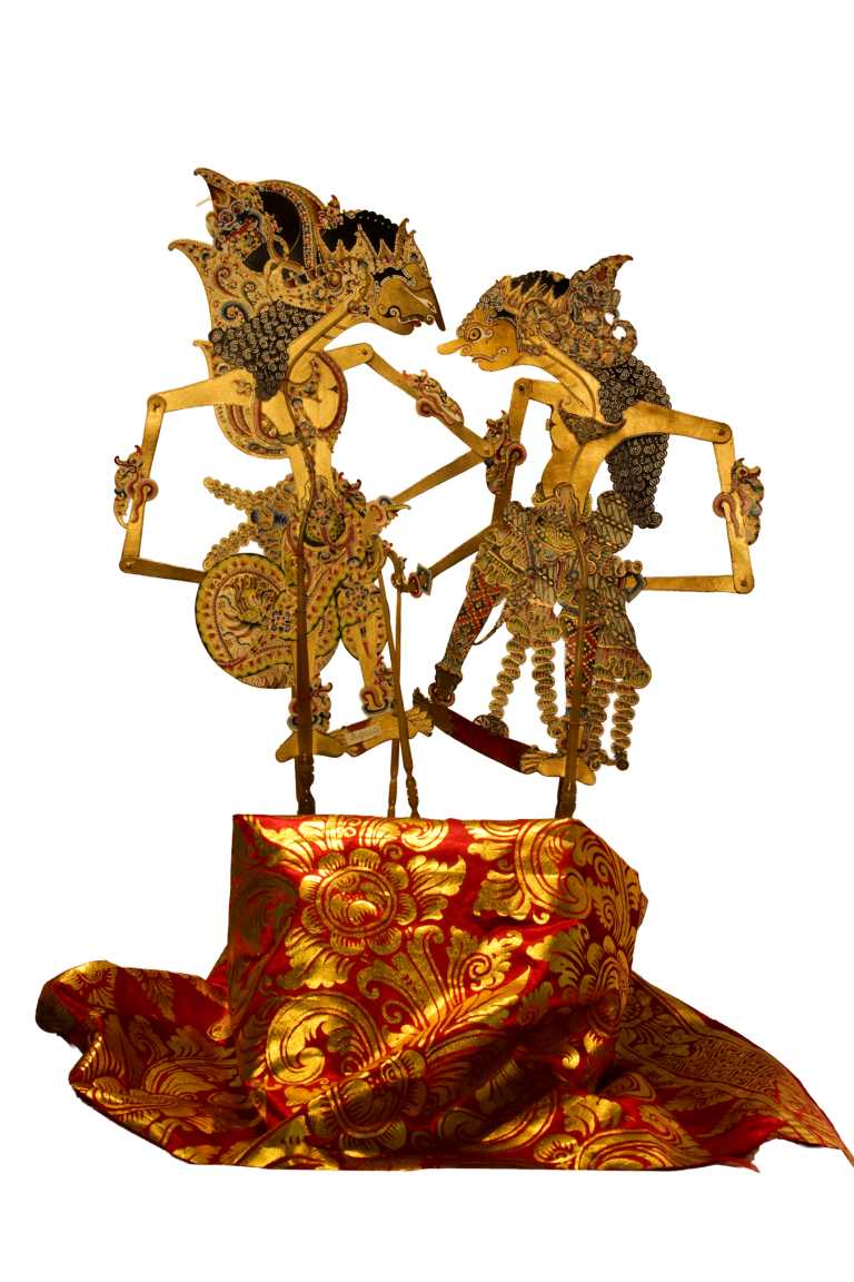 Dos figuras de wayang kulit enfrentadas sobre un textil rojo y dorado.