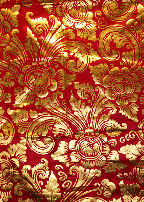 Detalle de un textil rojo con grandes motivos florales dorados.