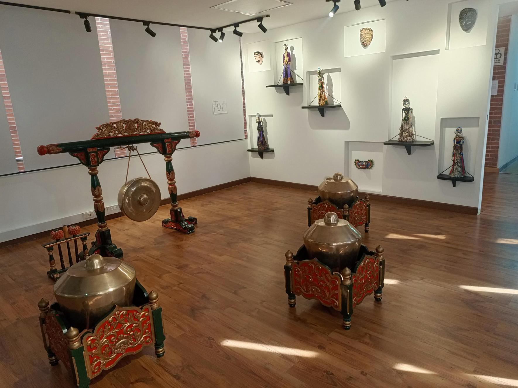 Vista general de la sala con el kenong al fondo, dos kempul en el centro y máscaras y marionetas en los nichos del muro.