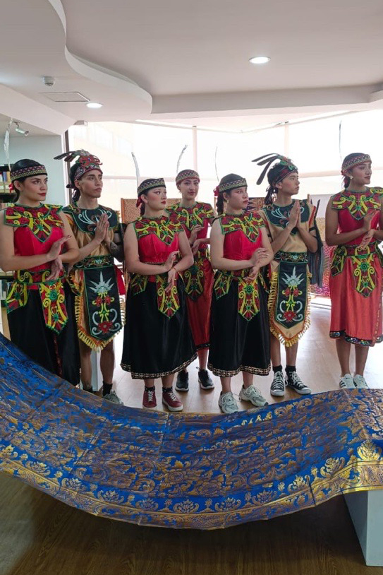 Grupo con trajes rojos y negros, de pie tras un gran textil azul y dorado.